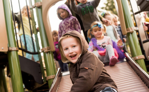 preschoolers sliding on slides, smiling, laughing and having fun