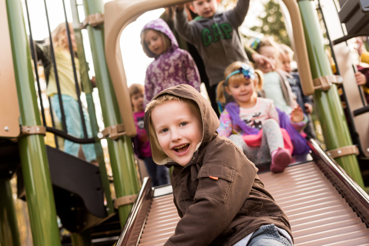 preschoolers sliding on slides, smiling, laughing and having fun