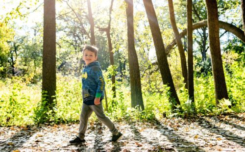 little boy walks smiling through the woods